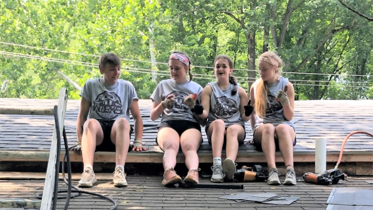 Young people take a break while sitting on a roof during a work camp day.